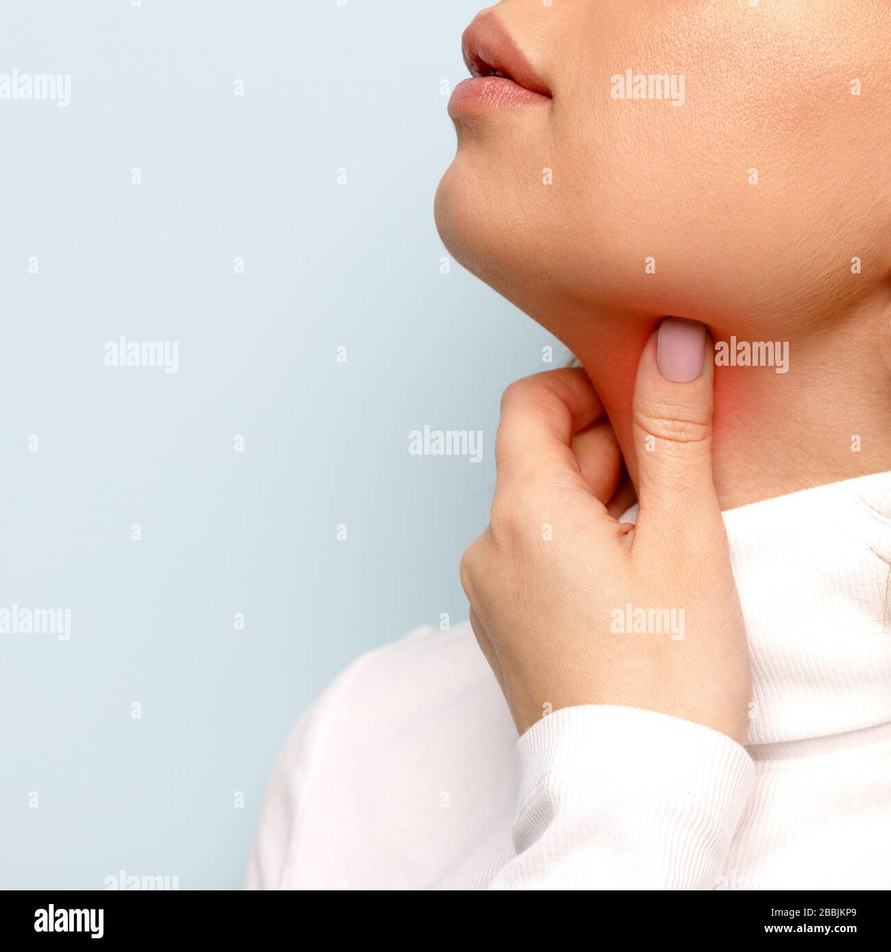 Close up of woman touches fingers of sore throat, isolated on blue background. Thyroid gland, painful swallowing, tonsillitis, laryngeal swelling conc Stock Photo