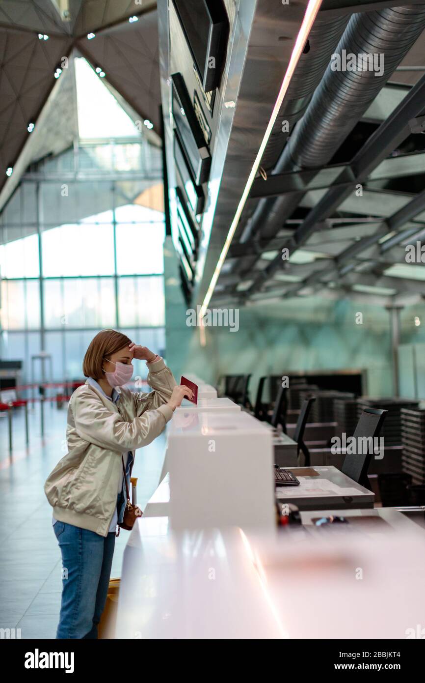Woman with luggage over flight cancellation, stands at empty check-in counters at airport terminal due to coronavirus pandemic/Covid-19 outbreak trave Stock Photo