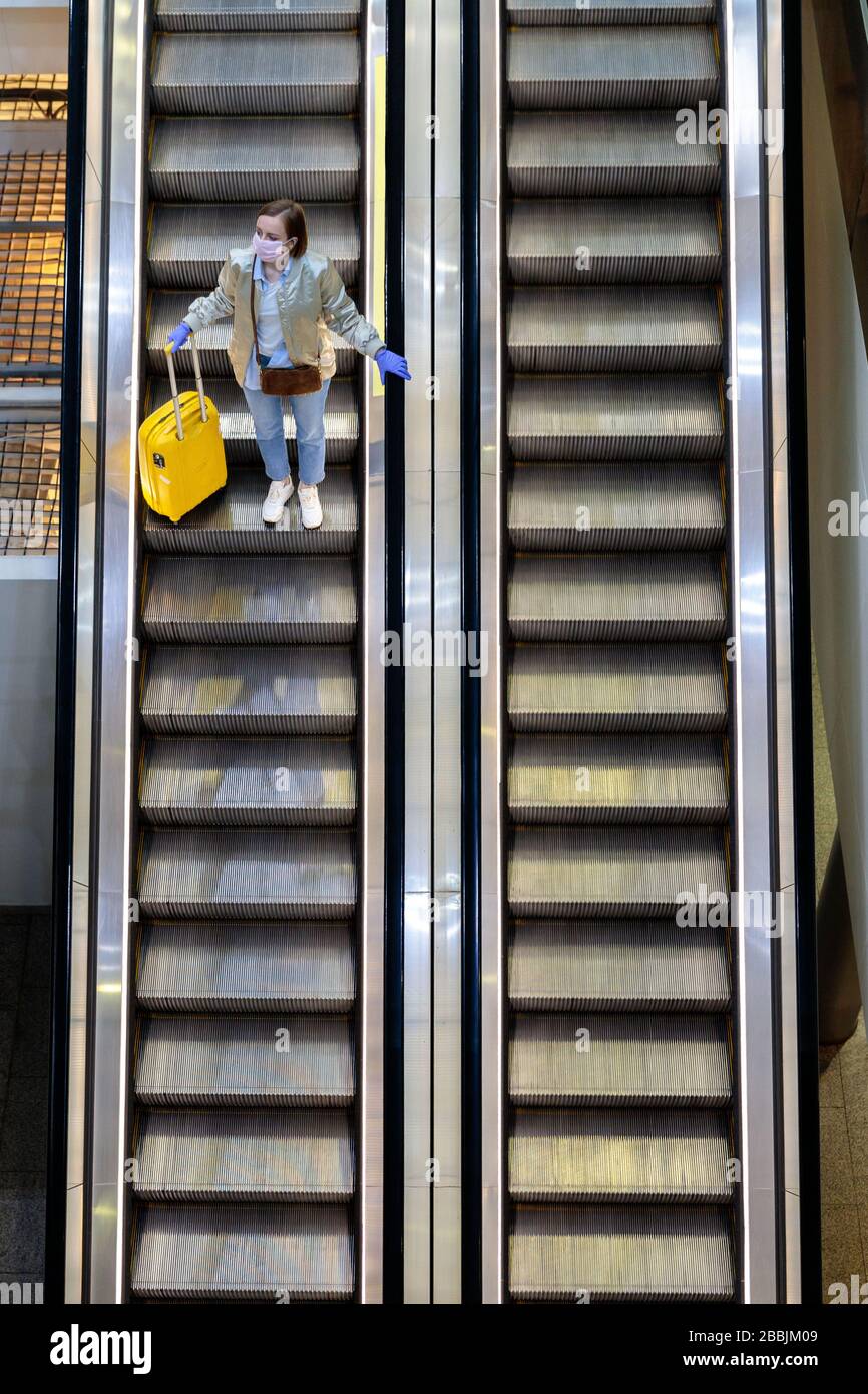 Woman with yellow luggage stands on escalator at almost empty airport terminal due to coronavirus pandemic/Covid-19 outbreak travel restrictions. Flig Stock Photo