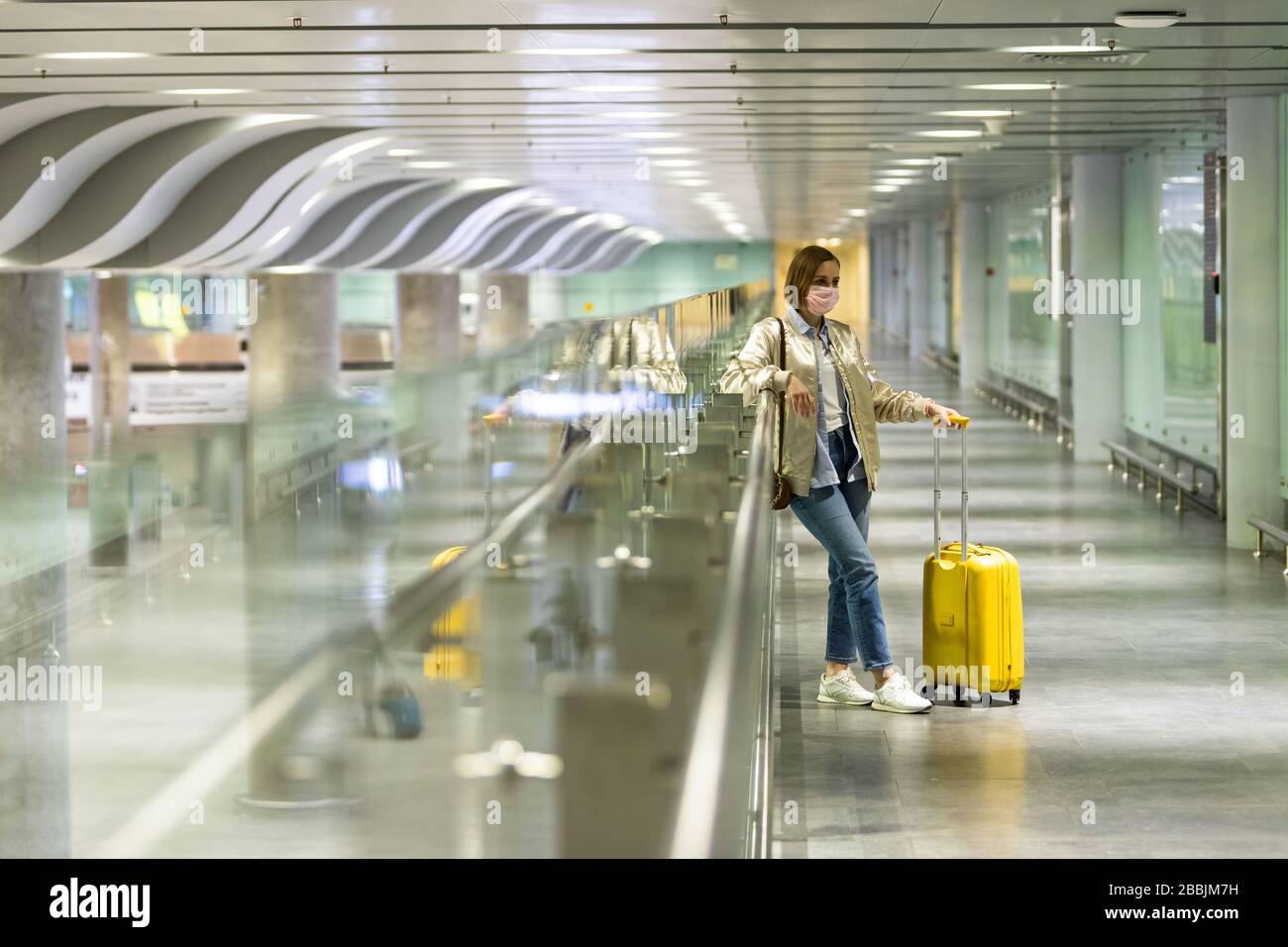 Woman with luggage stuck at empty airport terminal due to coronavirus pandemic/Covid-19 outbreak travel restrictions. Flight cancellation. Travel indu Stock Photo