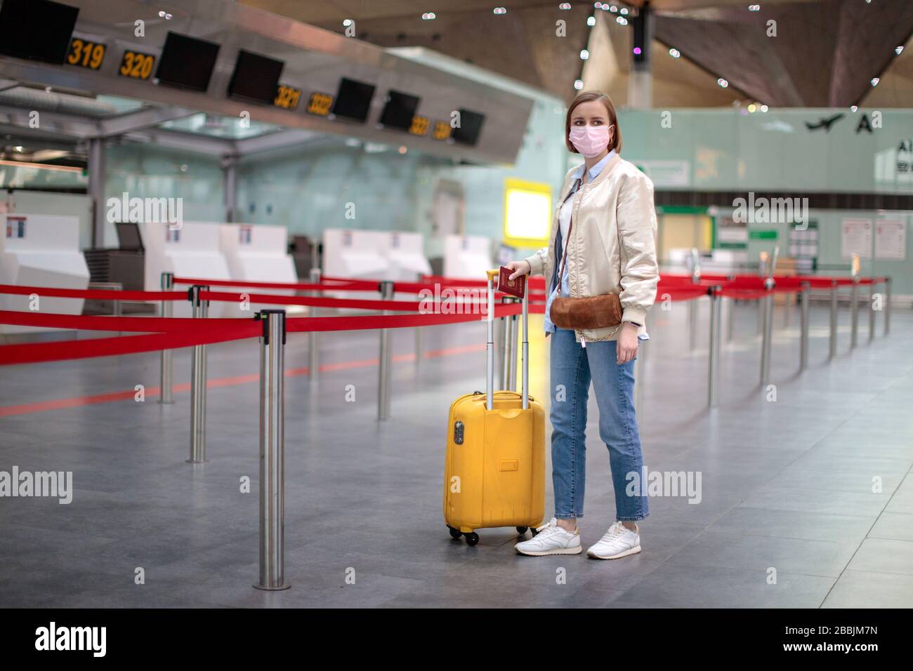 Woman with luggage stands at almost empty check-in counters at the airport terminal due to coronavirus pandemic/Covid-19. Flight cancellation. Travel Stock Photo