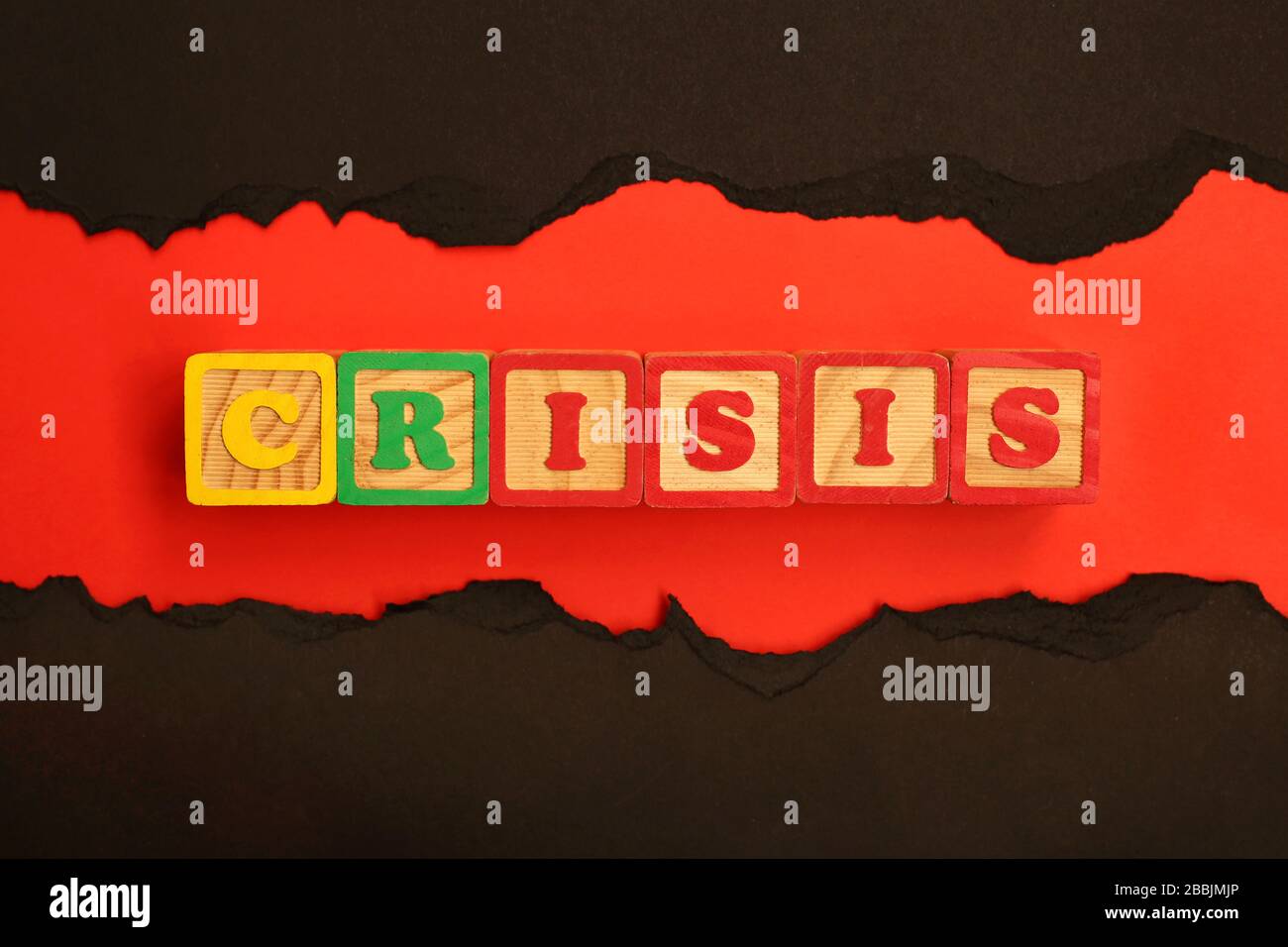 Word CRISIS made from wooden letters lies on a red and black background. Stock Photo