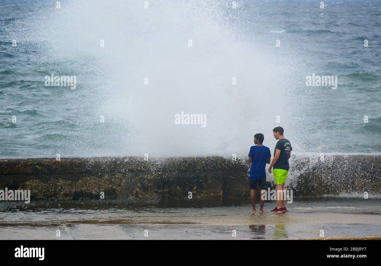 Stormy day blows waves over the Malecon, young people enoying the spray, Centro, Havana, Cuba Stock Photo