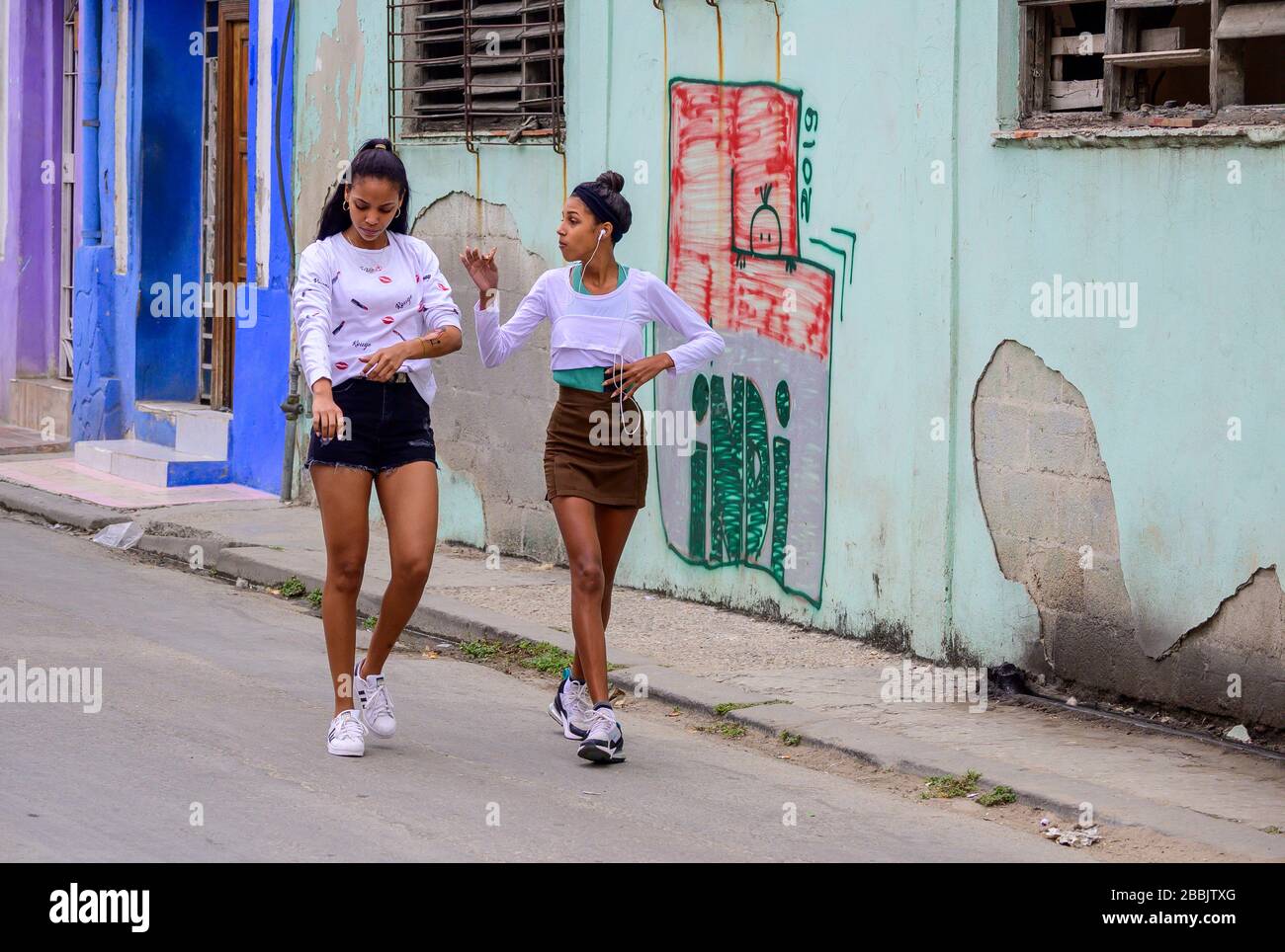 Young women walk past colorful walls, Havana, Cuba Stock Photo