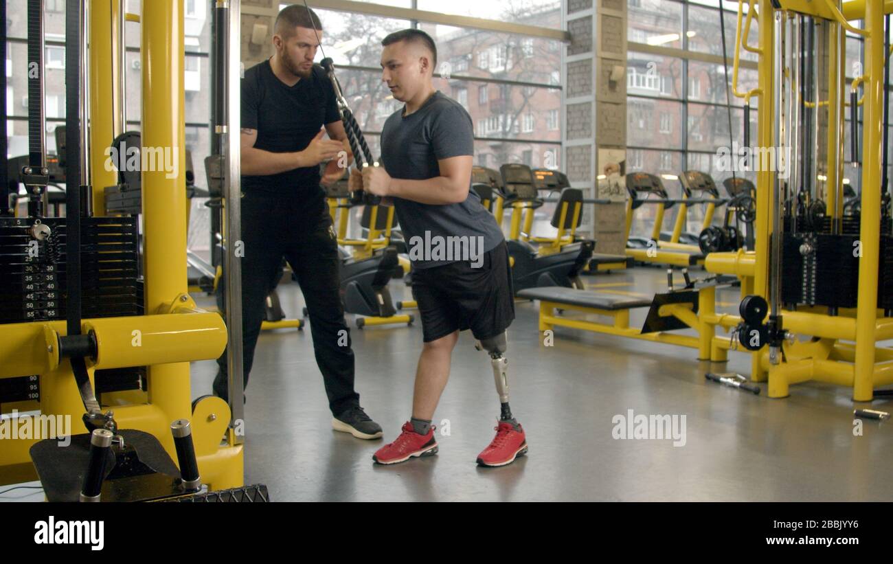 Disabled young man with instructor working out in gym Stock Photo
