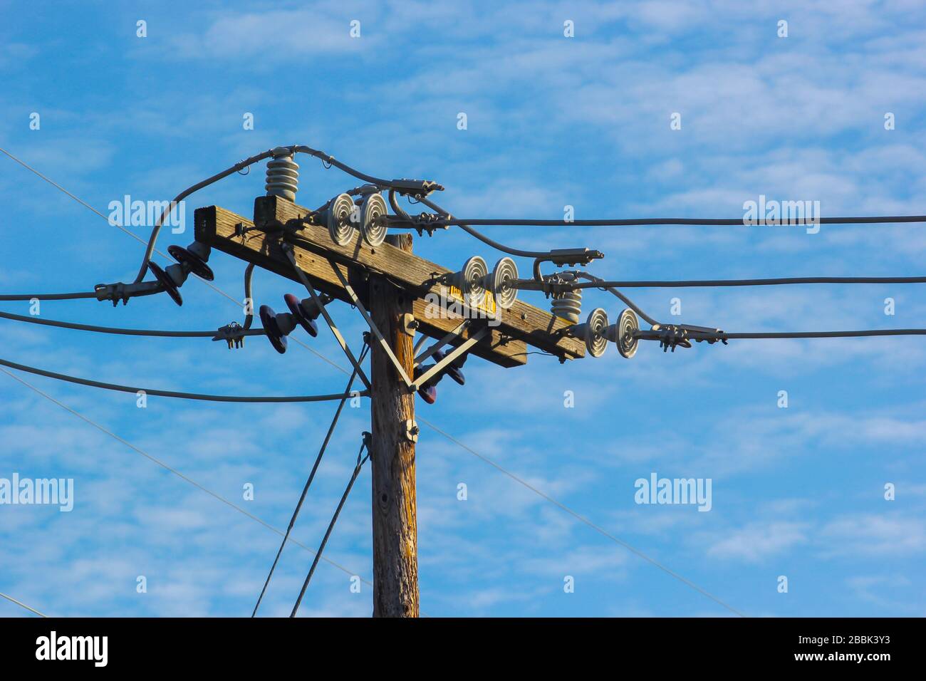 A towering electricity pole against a blue sky with white clouds Stock Photo