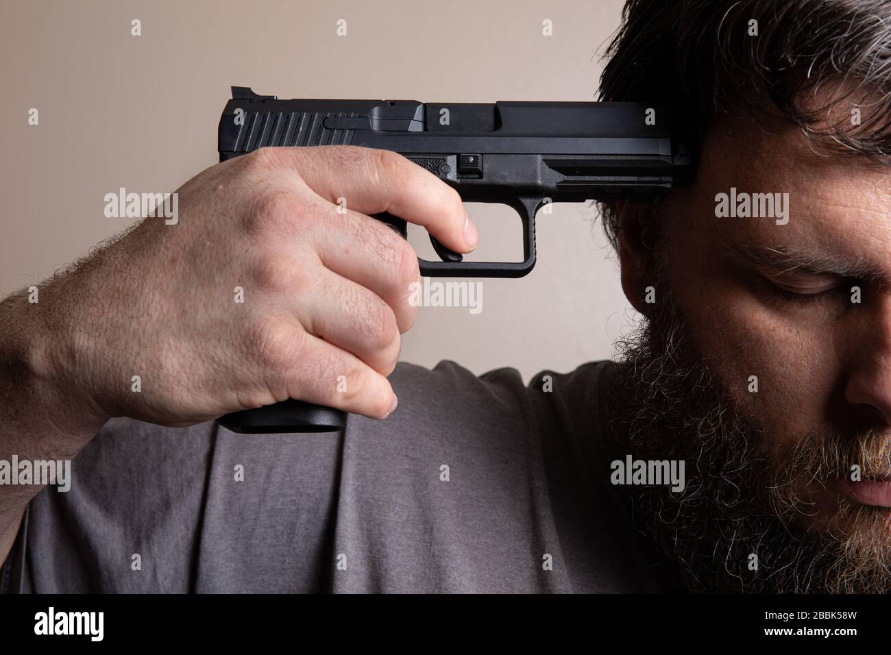 man with his head down holding a gun to end it Stock Photo