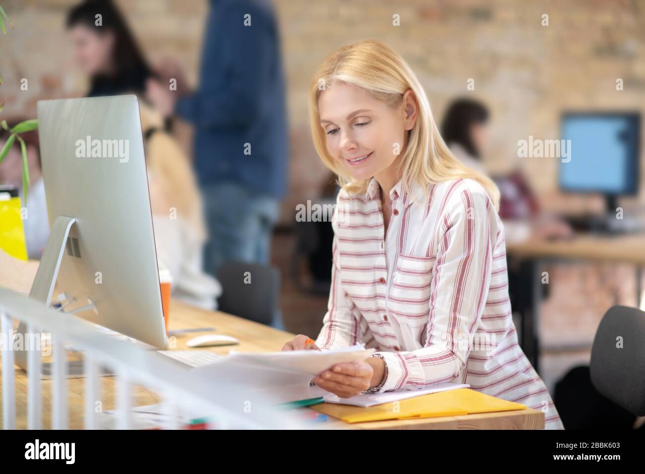 Blonde woman sitting at desk, checking notes Stock Photo