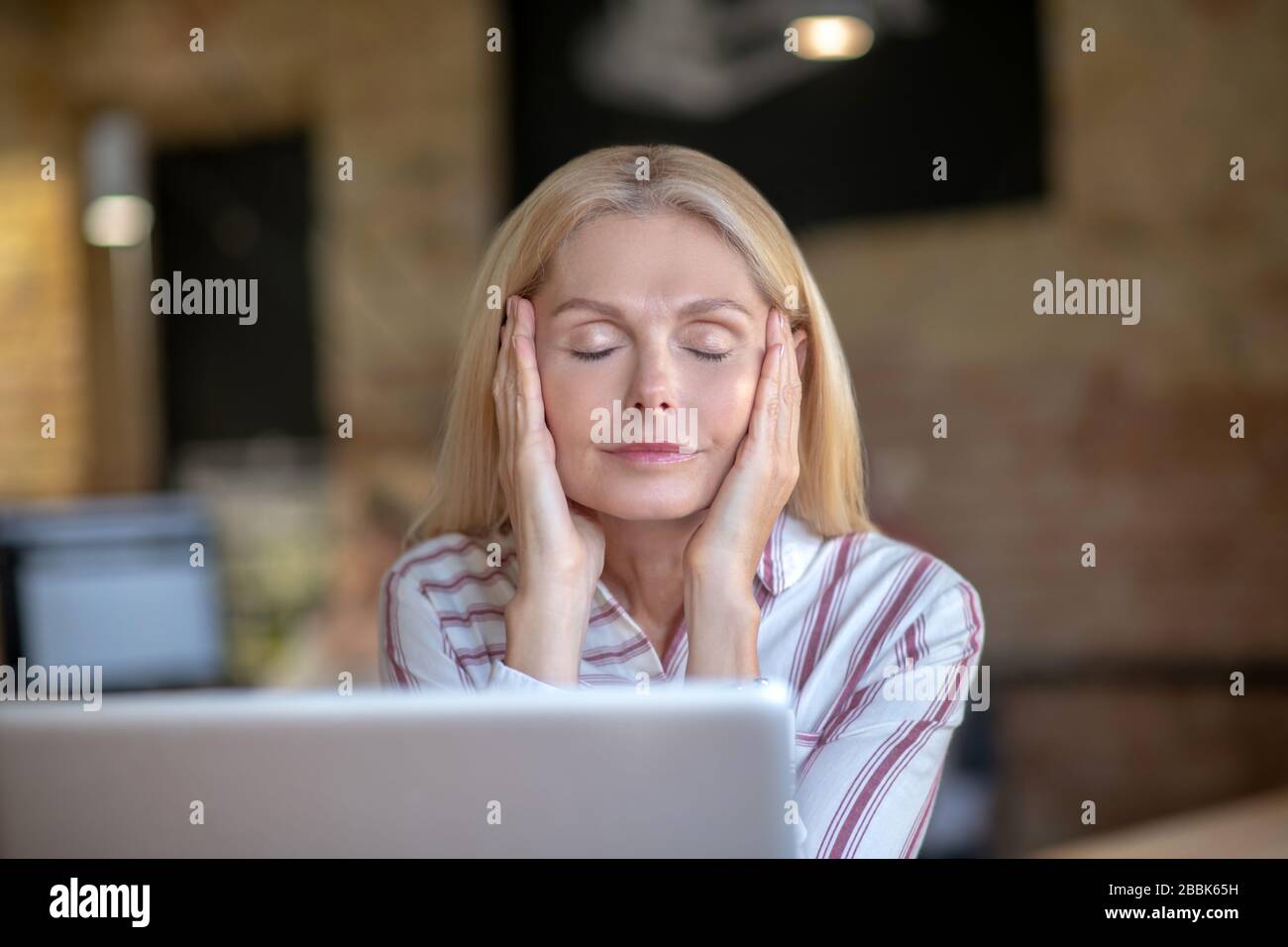Tired blonde woman sitting in front of laptop, holding temples Stock ...