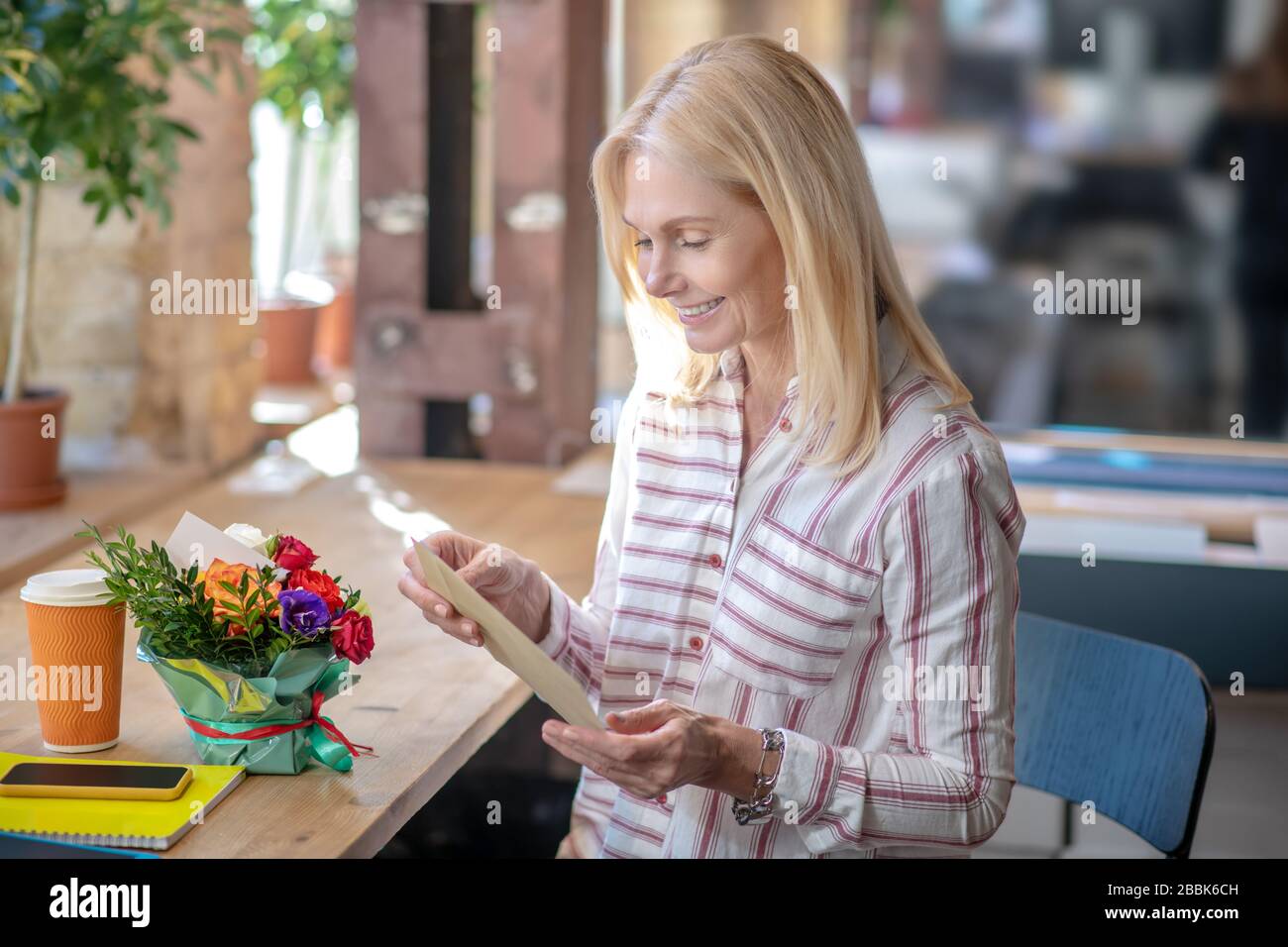 Blonde woman receiving letter and flowers, feeling happy Stock Photo
