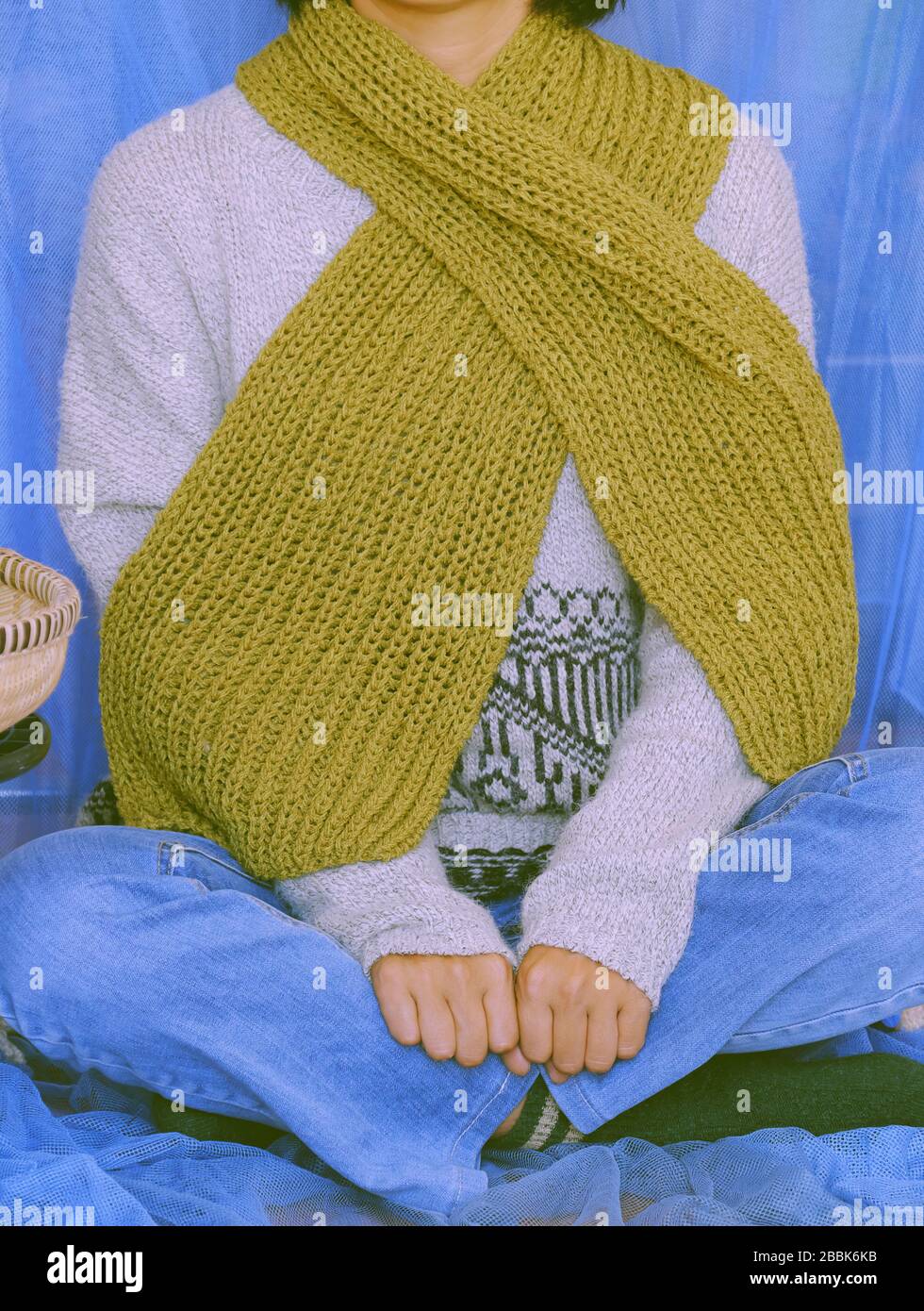 Woman wear blue jeans, white woolen sweater, sock and moss green wool scarf sit with blue background, knitted handmade product to make warm for winter Stock Photo