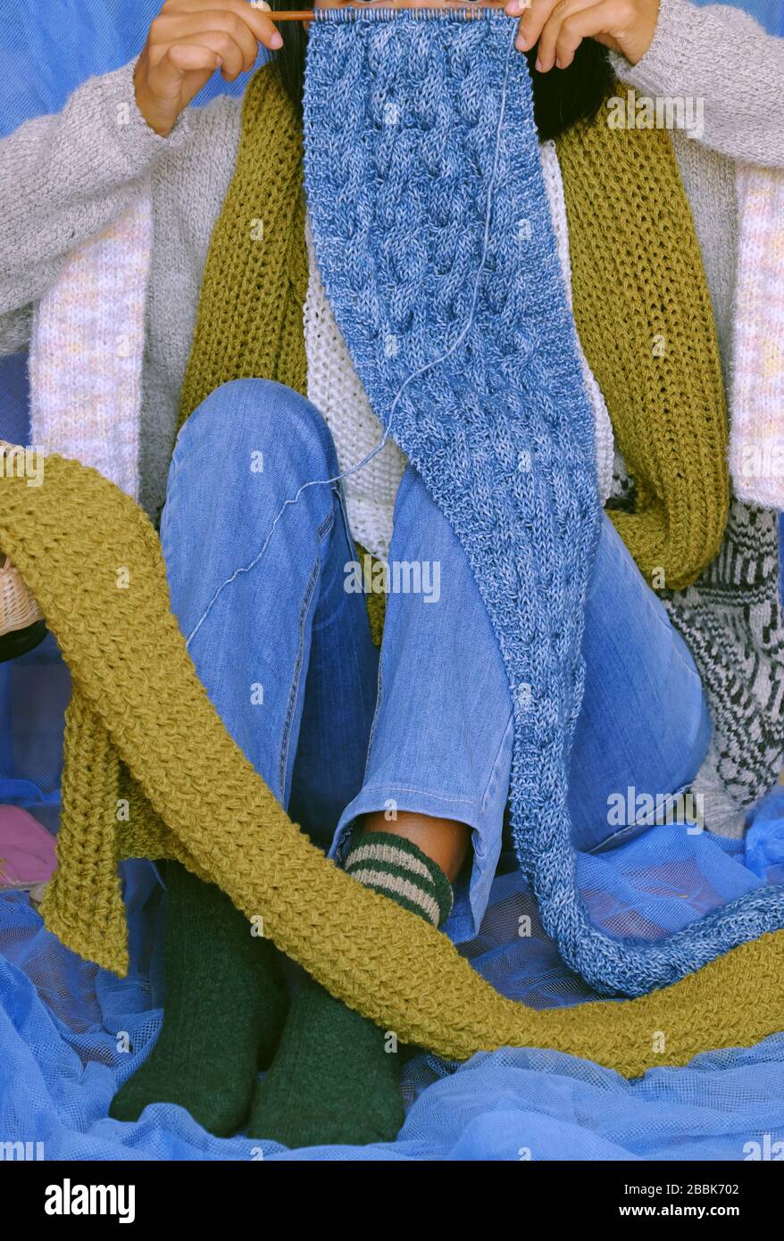 Concept woman wear blue jeans, white woolen sweater, sock, moss green wool scarf on blue background, hand knit handmade present make warm for winter Stock Photo