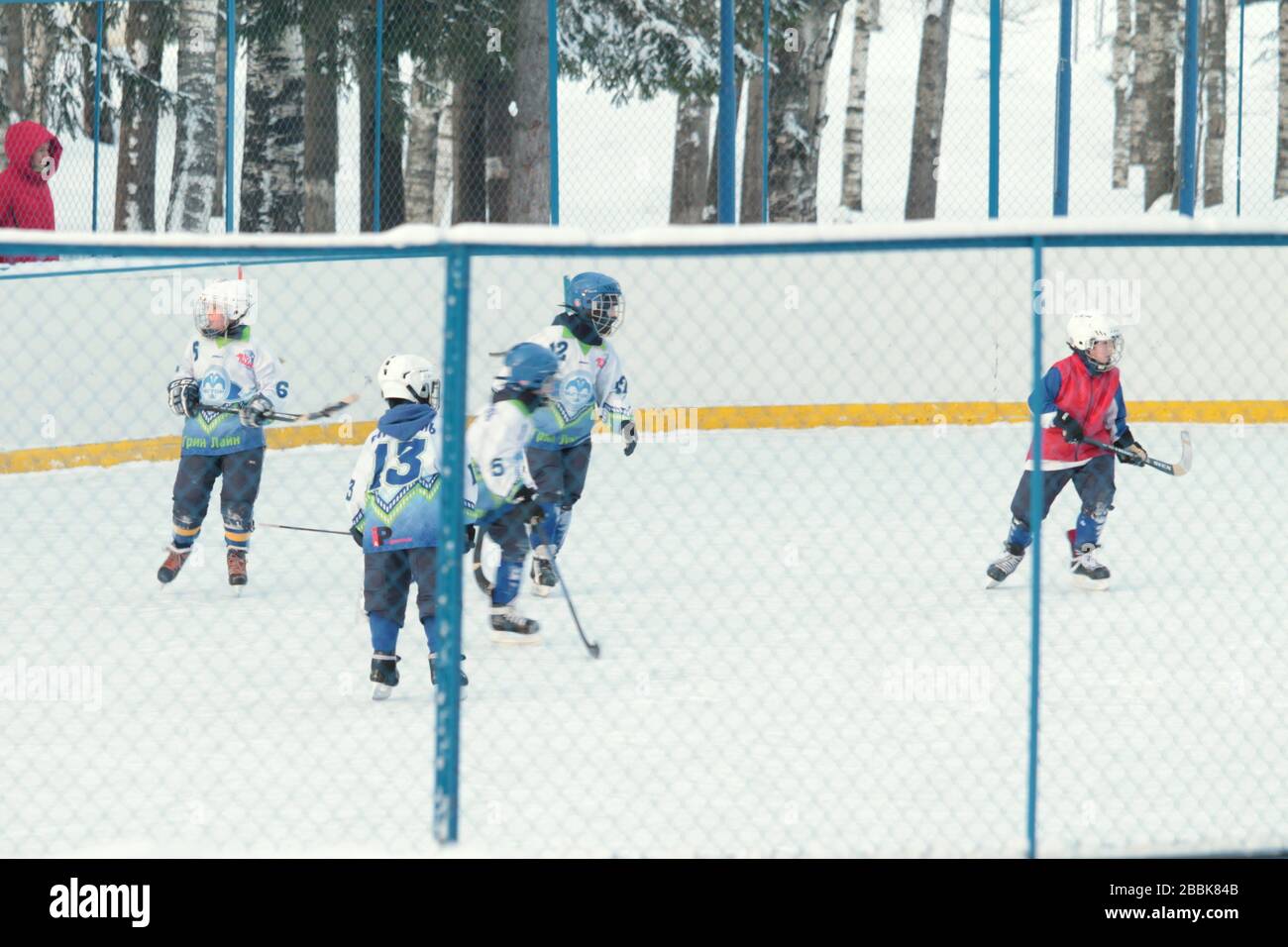 People in red and blue sports gear play hockey in park. Winter season