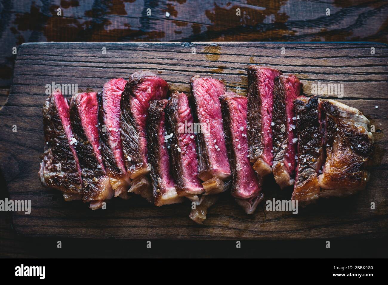 Delicious homemade medium rare black Angus sliced steak with sea salt on a wooden board top view American food Stock Photo