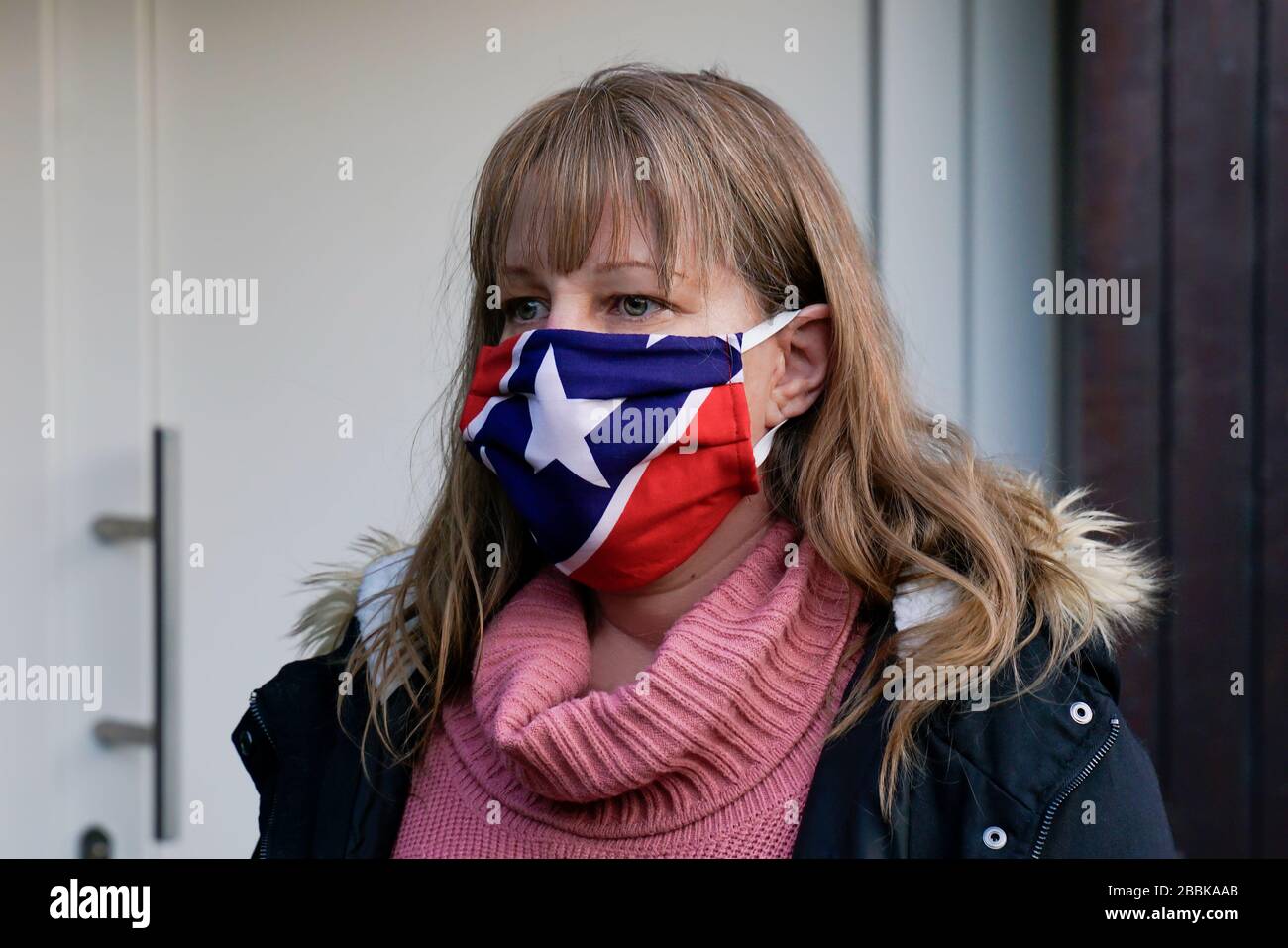 A 40 year old blonde woman is wearing a fabric mask. It protects against Corona Virus. Homemade mask made of fabric with stars and stripes. Stock Photo