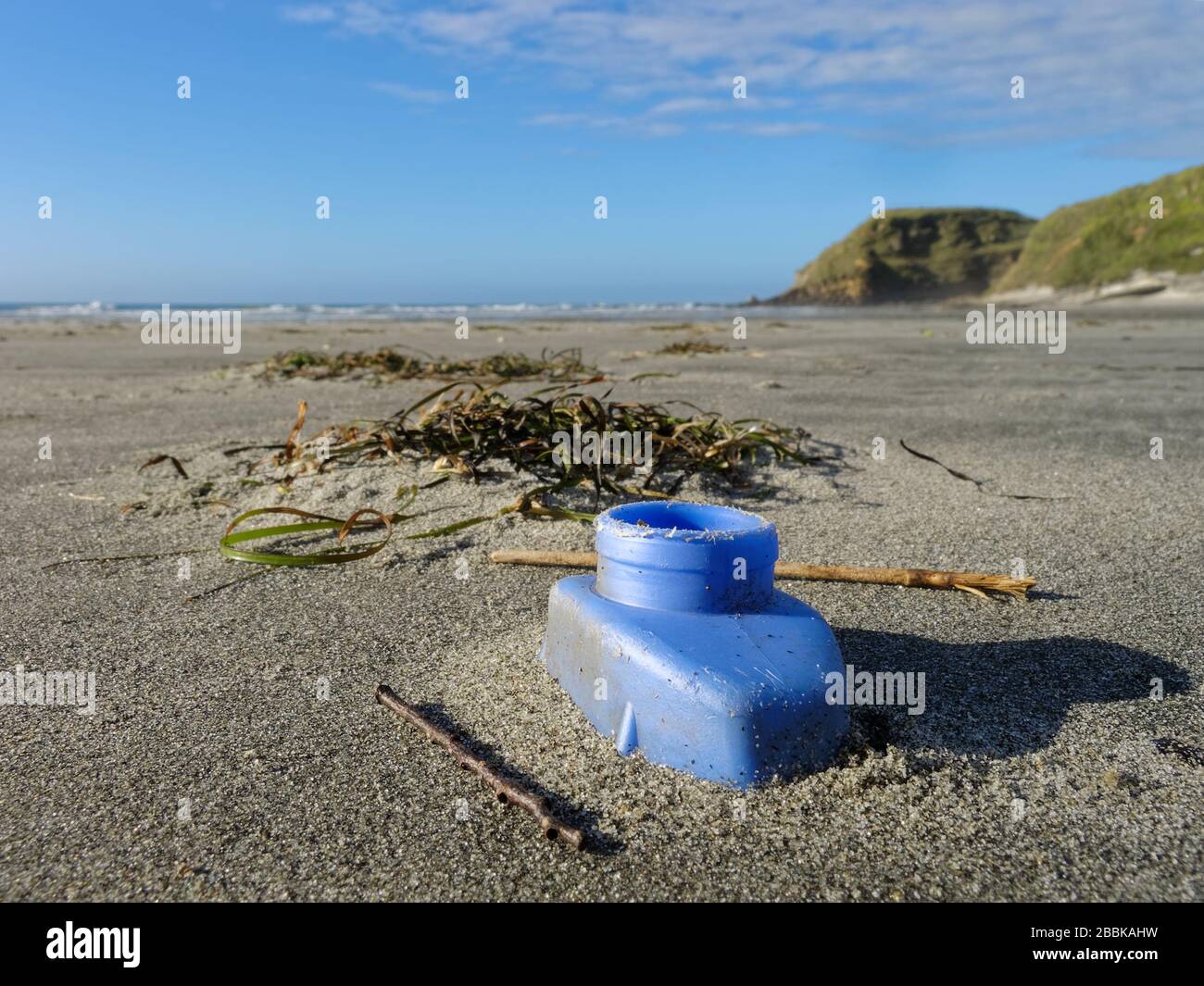 Discarded blue plastic bottle part buried on a beach on New Zealand's west coast. A deathtrap for small creatures. Stock Photo