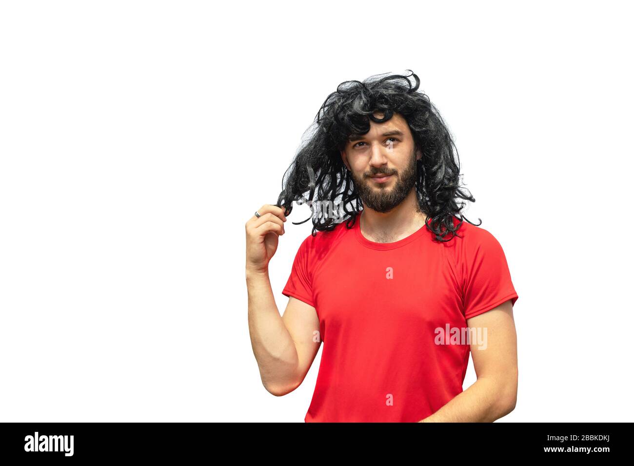 Handsome smiling bearded man in wig of curly long messy hair and red t-shirt isolated on white. Copy space. Exotic hair-do. Time to visit barbershop. Stock Photo