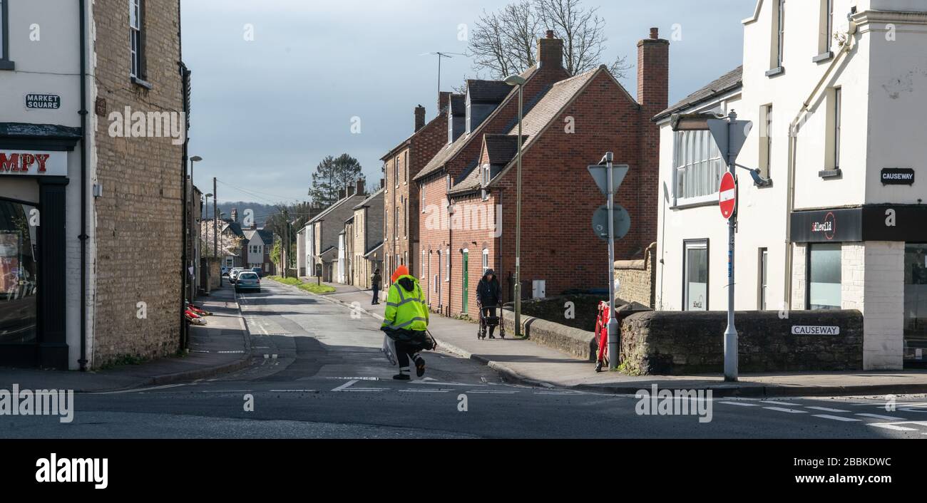 A street cleaner providing essential services walks across a deserted intersection. Covid times. Bicester Town Centre, Oxfordshire, UK Stock Photo