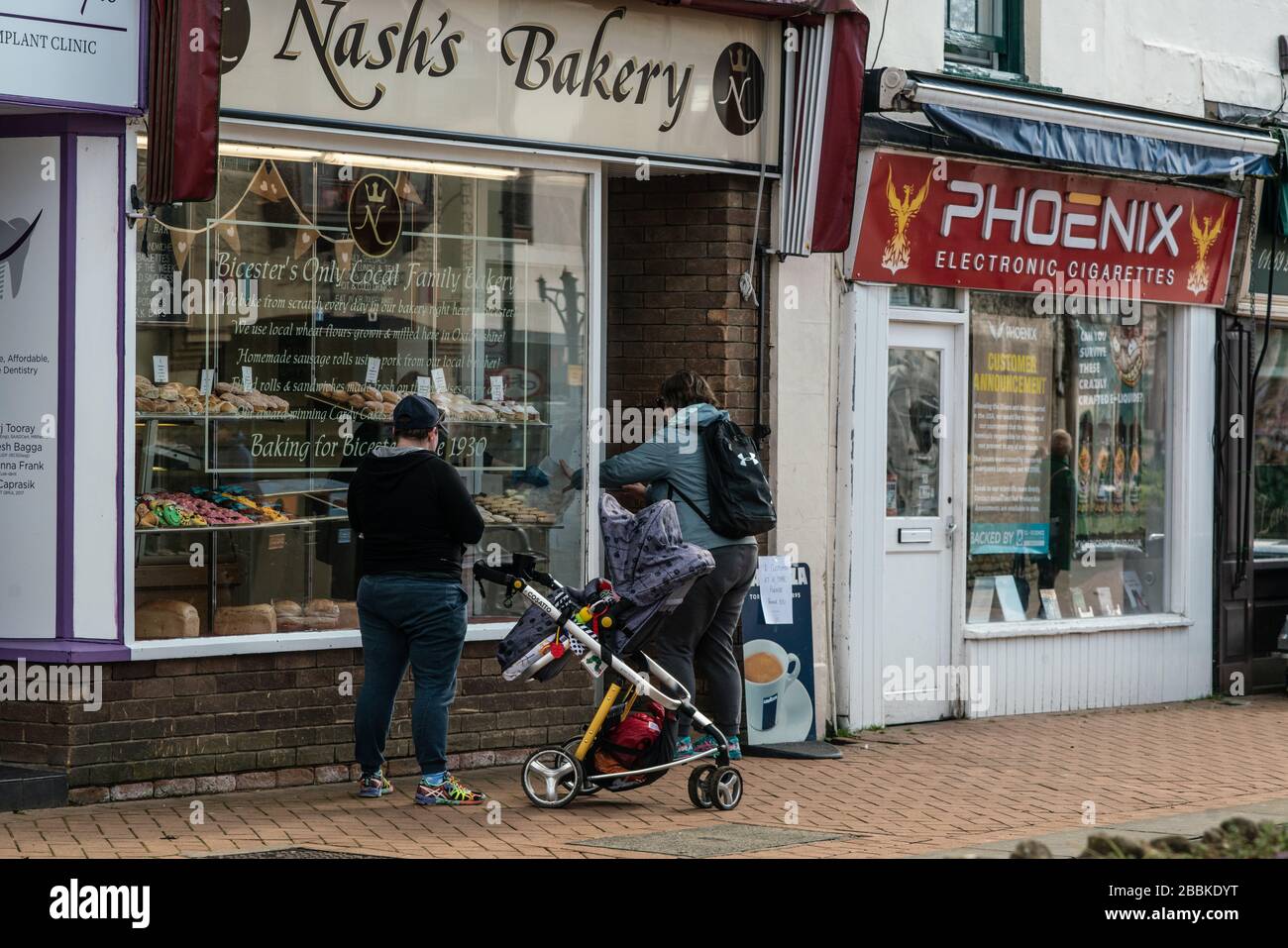 A woman collects a bakery order from outside the shop, due to social distancing measures put in place by government during the UK lockdown. Stock Photo