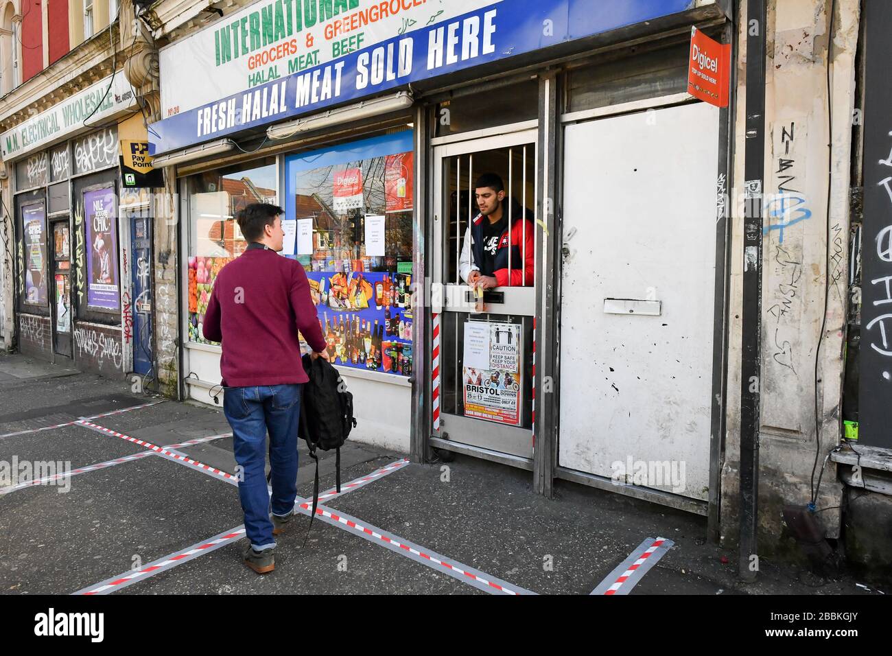 A man buys a drink from a modified shop door that has been transformed into a serving hatch by removing the glass and metal bars in St Pauls, Bristol, as the UK enters the second week of lockdown due to the global coronavirus pandemic. Stock Photo