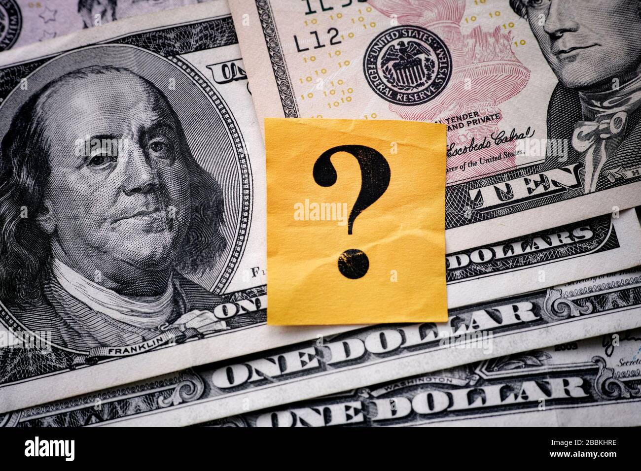Yellow paper note with question mark on US dollar background. Close up