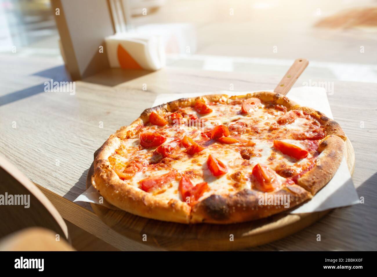 Big pizza stands on a table in a cafe. Italian pizza cut on pieces. Stock Photo