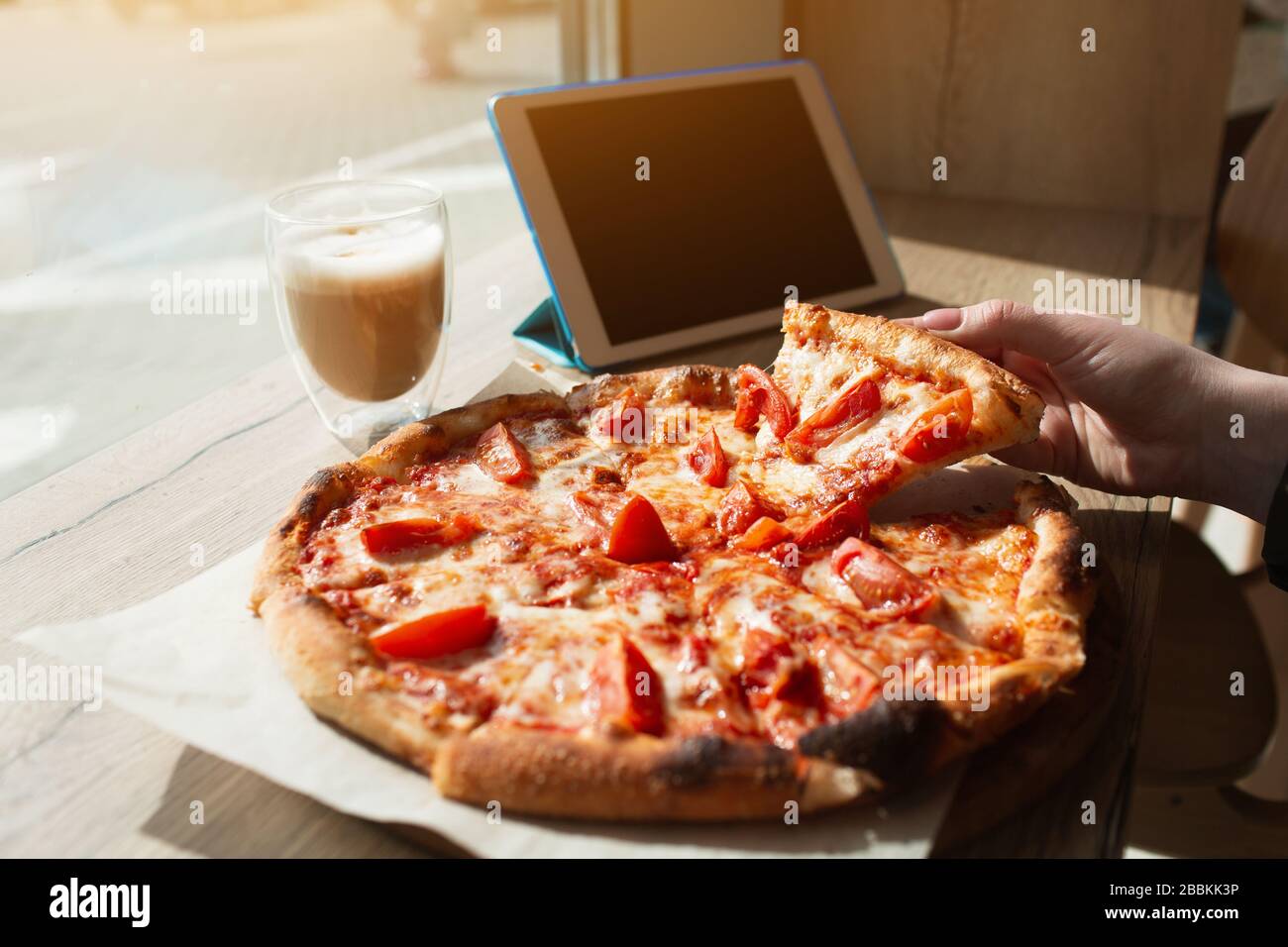 Big pizza stands on a table in a cafe. Hand taking a piece of pizza close-up. Stock Photo