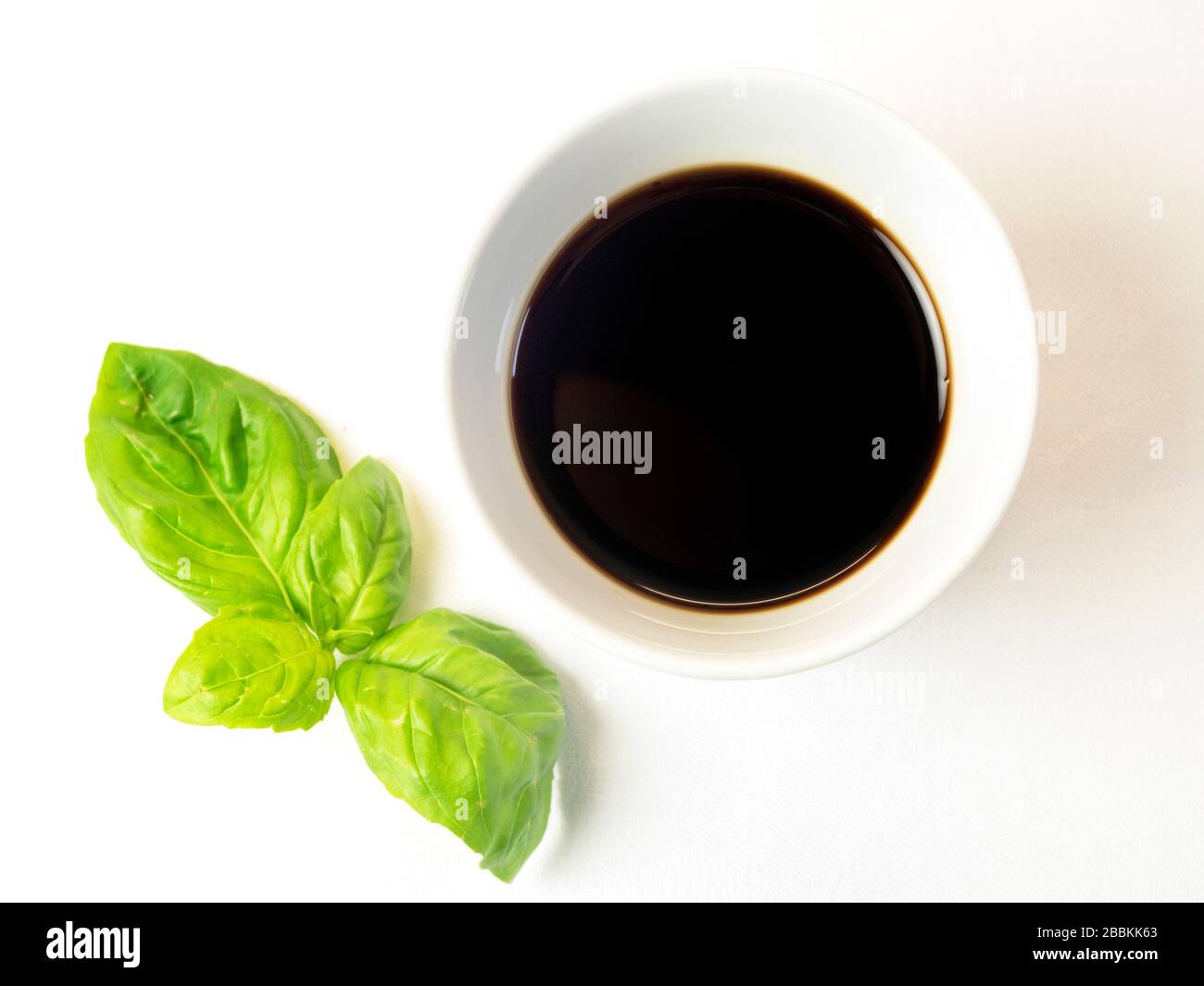 A small bowl of balsamic vinegar with a sprig of basil on a white tablecloth Stock Photo