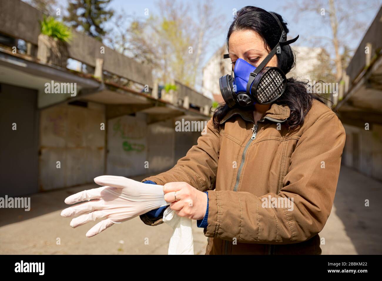 Woman with filter mask on her face puts rubber gloves on her hands for ...