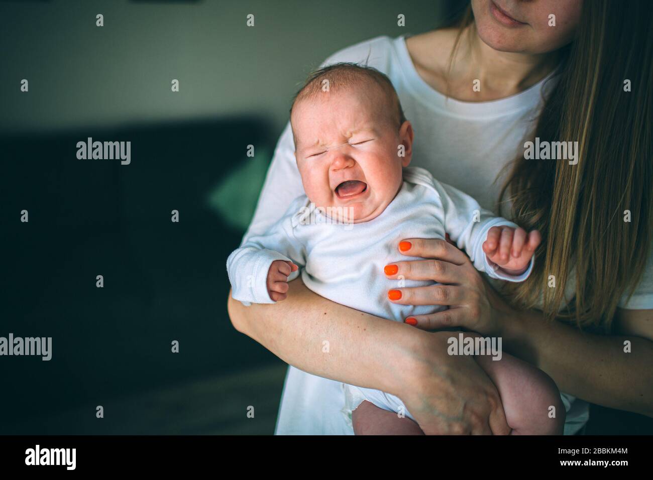 Portrait of a newborn baby. Mother holds a child in her arms. A newborn is screaming. Stomach pain, childhood cramps. Crying newborn baby. The first Stock Photo