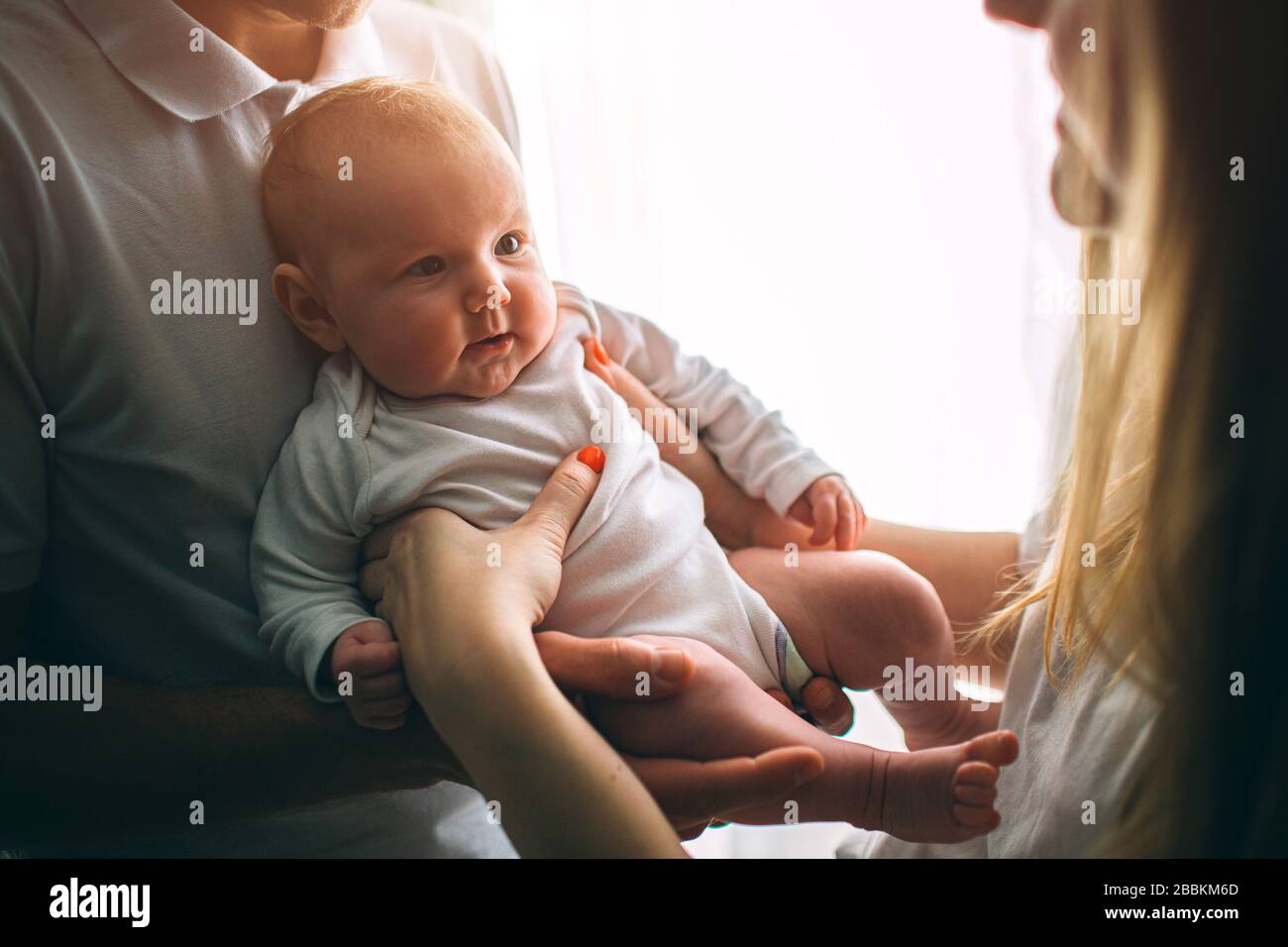Mother and father are holding a baby in their arms. Care and health. Happy young family. Stock Photo