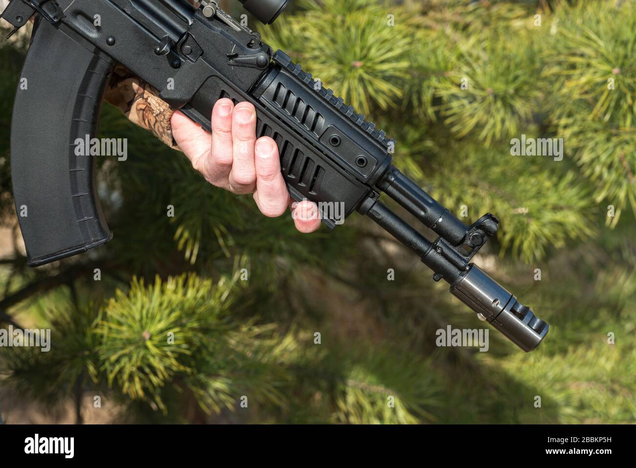 A man is holding a rifle camouflage clothes pine background Stock Photo