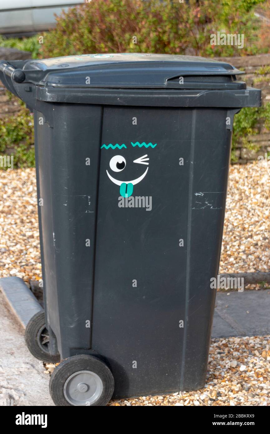 a close up view of a black wheeling rubbish bin with a funny face sticker on the side Stock Photo