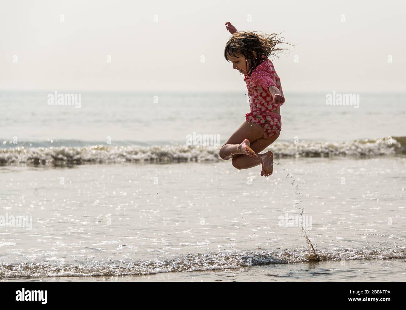 Young girl jumping in the waves at the seaside, splashing and having fun. Camber sands, England Stock Photo