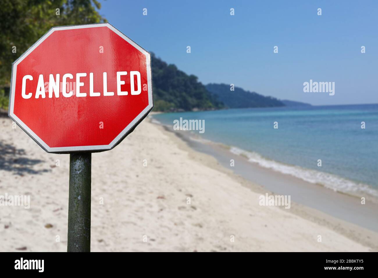 Red cancelled sign on beach background. COVID-19 pandemic quarantine. Cancelled vacation, travel, holiday plans because of corona virus. Stock Photo