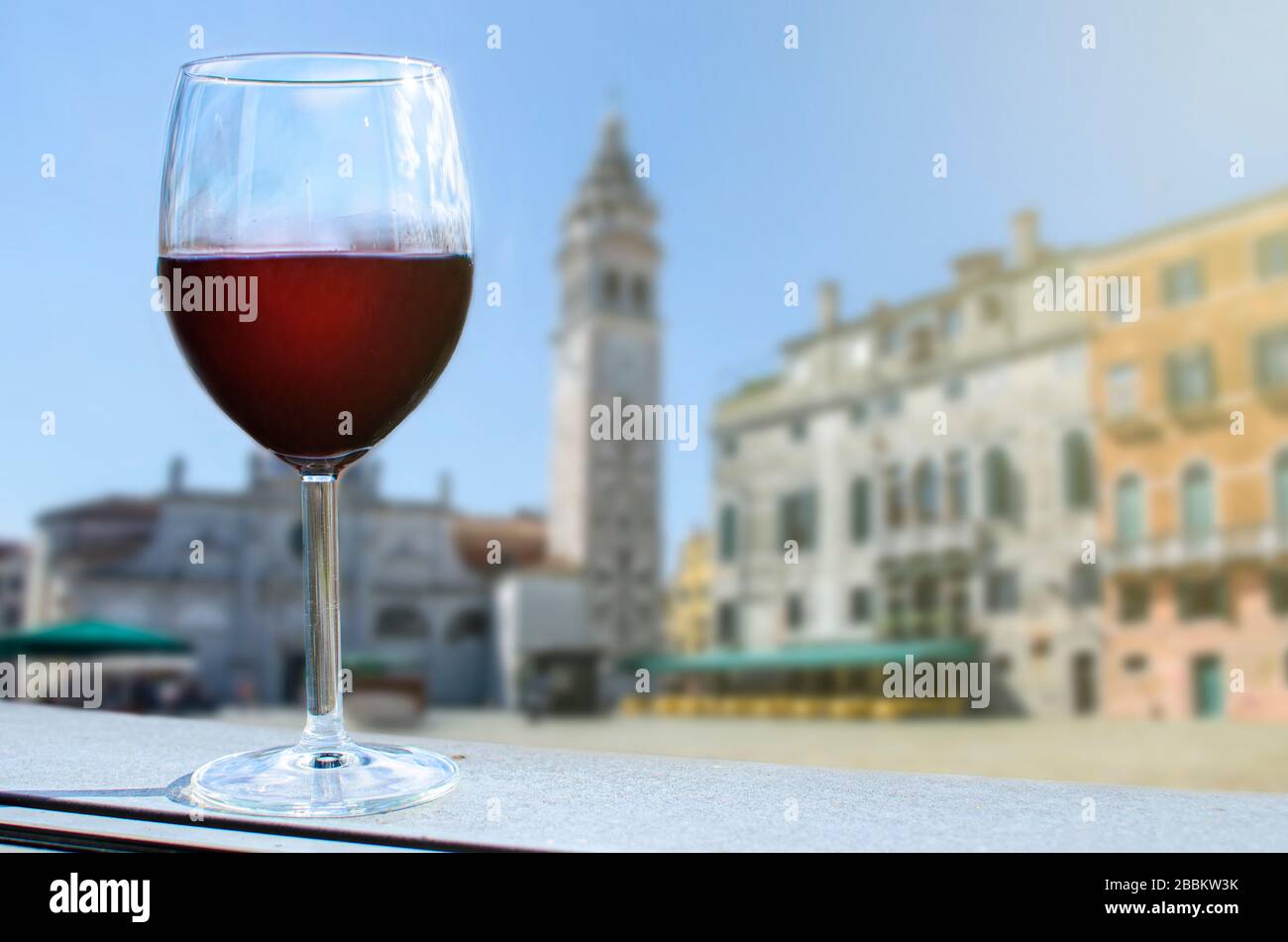 Glass of red wine on the table and Italian square in Venice with tower