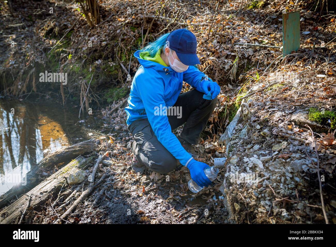 Ecologist taking water samples from a natural source in protective gloves and mask Stock Photo