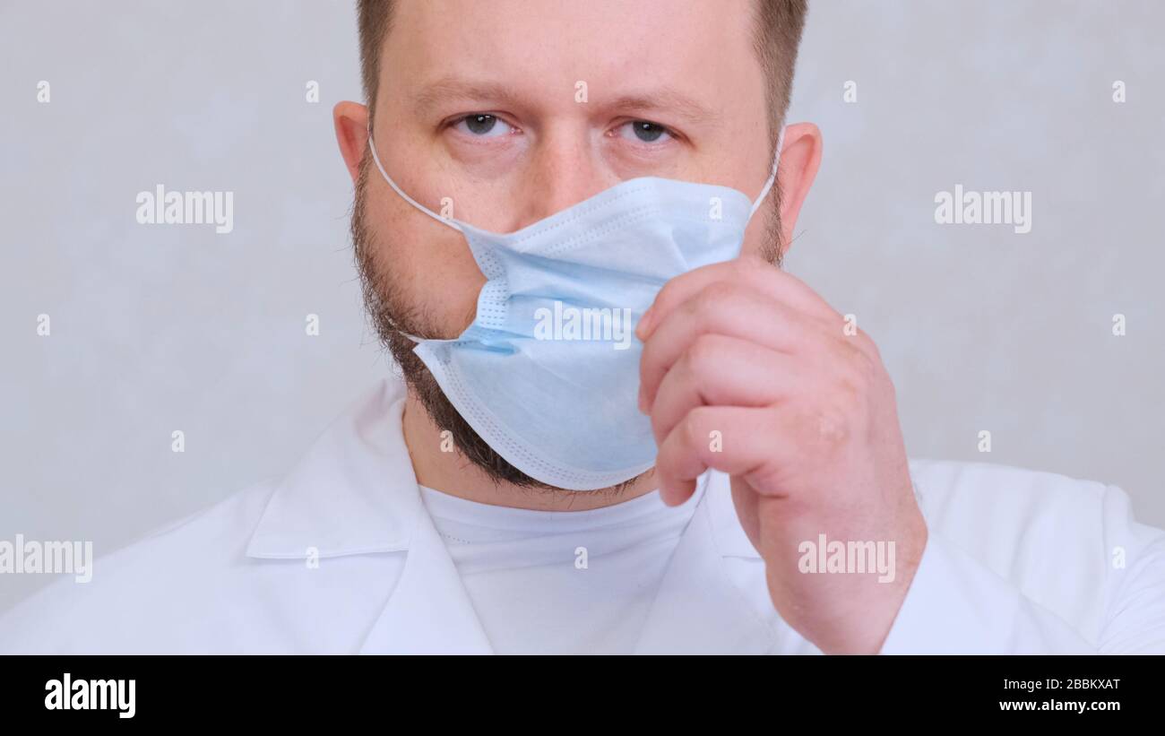 bearded male doctor takes off his protective mask with a sad look. This ...