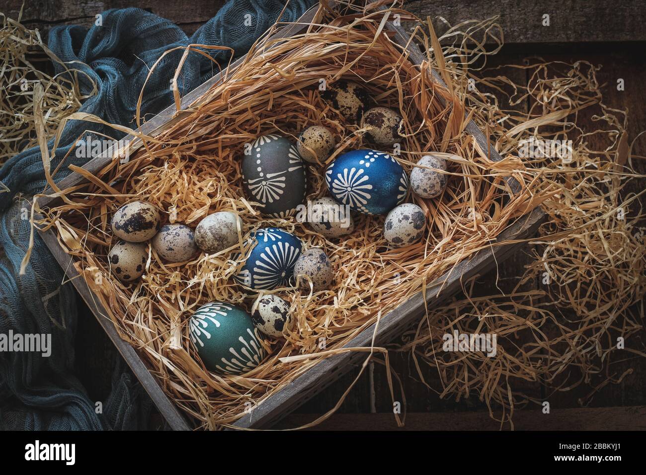 Quail eggs and colorful wax decorated chicken eggs in a box on a hay. Easter composition in a dark mood Stock Photo