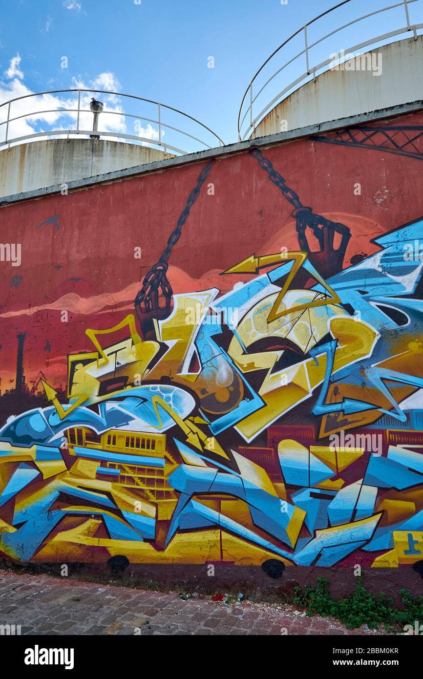 Graffiti painted on a stone wall with 3 oil storage tanks behind at the Quai de Sénégal in the redevelopment area of Bacalan-Bassins à Flot, Bordeaux Stock Photo