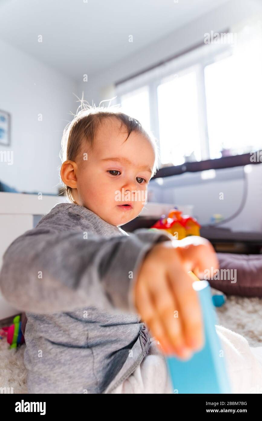 Portrait of one year old baby girl indoors in bright room playing by herself Stock Photo