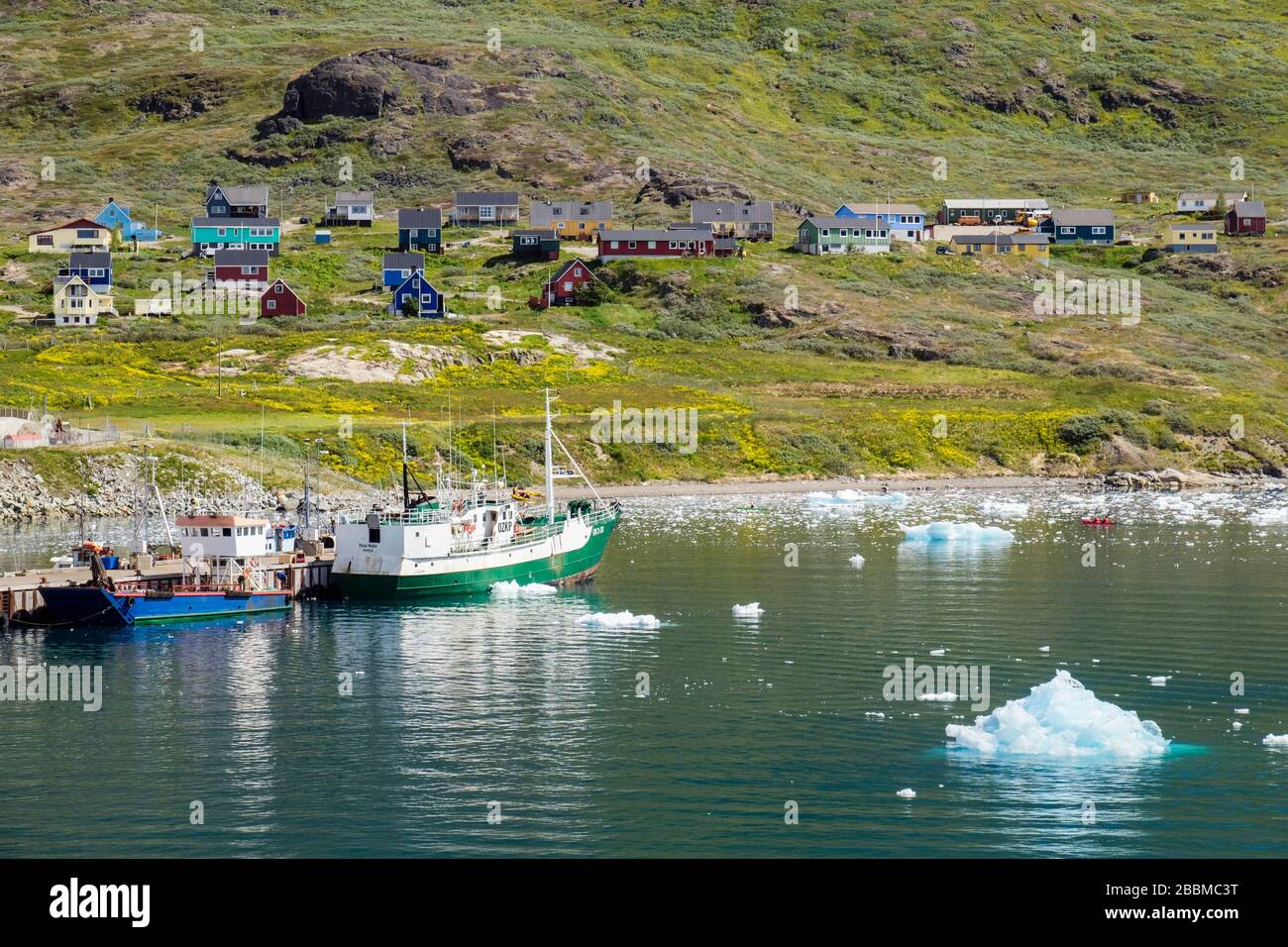 Offshore view to fishing boats in port with icebergs from Tunulliarfik Fjord and traditional houses on the hillside. Narsaq, Kujalleq, South Greenland Stock Photo