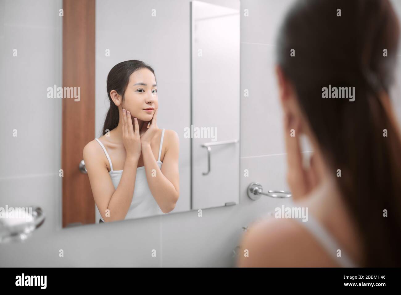 Beauty in mirror reflection. Over the shoulder view of beautiful woman touching her face while looking in the mirror Stock Photo