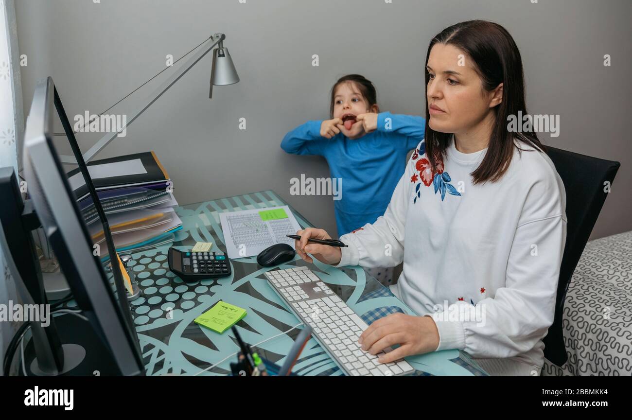 Woman telecommuting making a video conference with her daughter grimacing behind Stock Photo