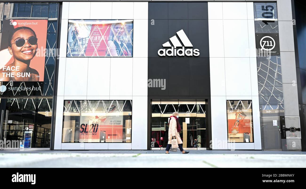 01 April 2020, Hessen, Frankfurt/Main: A woman walks past an Adidas store  on Frankfurt's Zeil shopping mile. The German sporting goods manufacturer  reaped a shitstorm after the announcement that it would not
