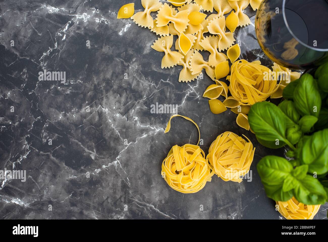 Dry pasta on black marble worktop with red wine & basil Stock Photo