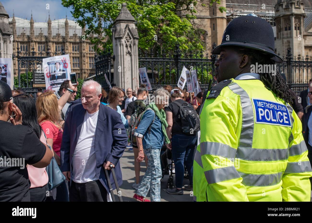 Police officer watches from a distance, as a 'Operation Shutdown' protest demonstration takes place at the gates to the House of Parliament in London. Stock Photo