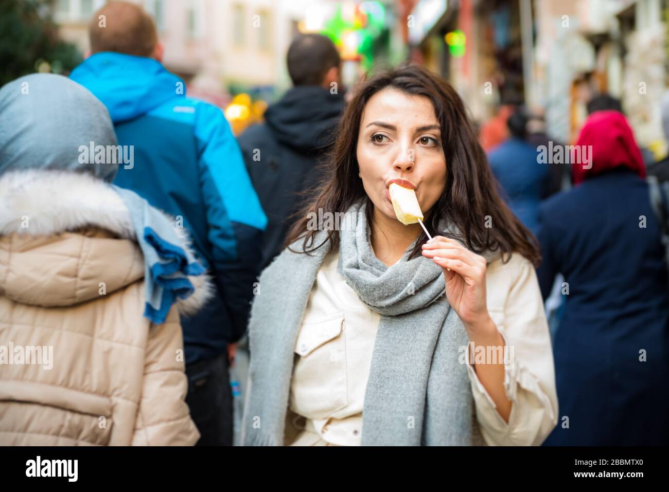 Beautiful young traveler woman in fashionable clothes enjoys eating piece of pineapple with a stick.Street food concept. Stock Photo