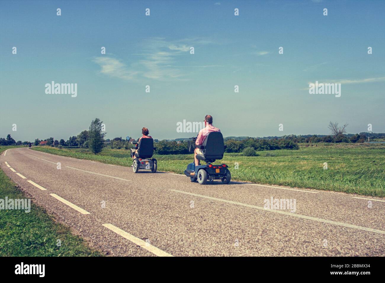 Couple in motorized wheelchairs on a road in the Netherlands in summer Stock Photo
