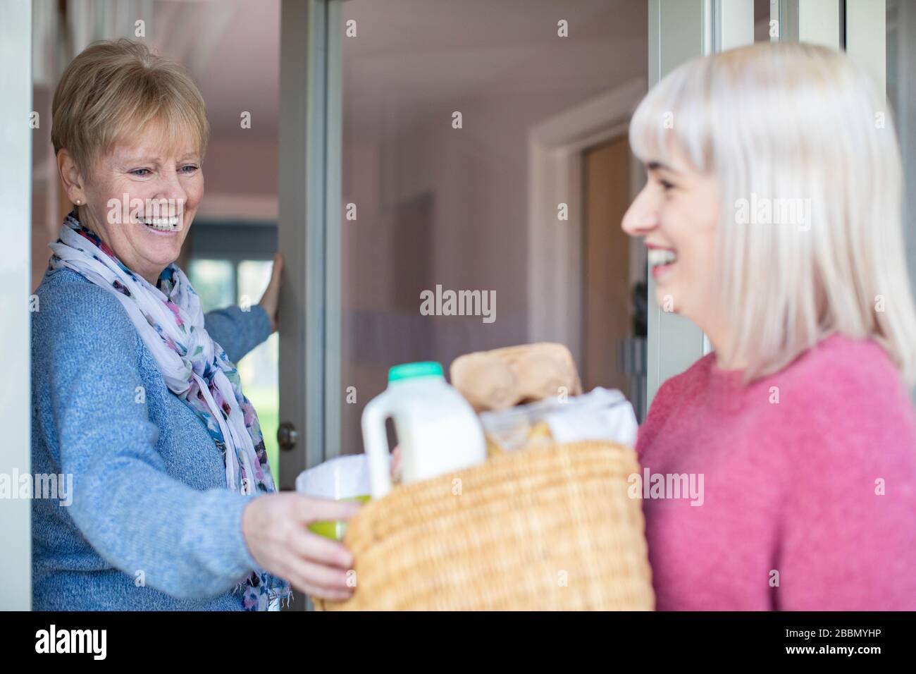 Female Neighbor Helping Senior Woman With Shopping Whilst Self Isolating During Coronavirus Stock Photo